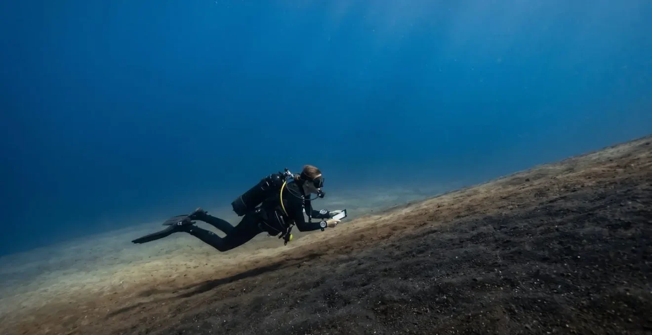 Scuba diver navigating along a featureless volcanic sand slope in Tenerife's clear blue waters