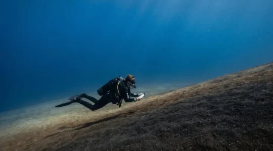 Scuba diver navigating along a featureless volcanic sand slope in Tenerife's clear blue waters