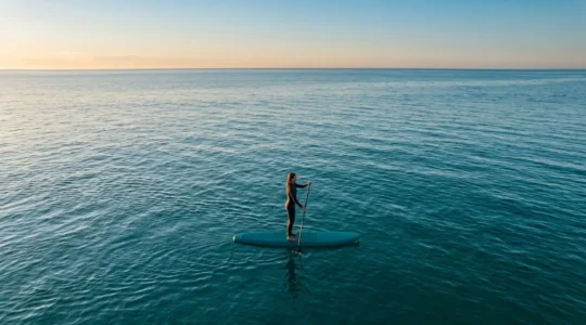 Stand-up paddleboarder maintaining perfect balance on calm water, demonstrating core stability for scuba diving training