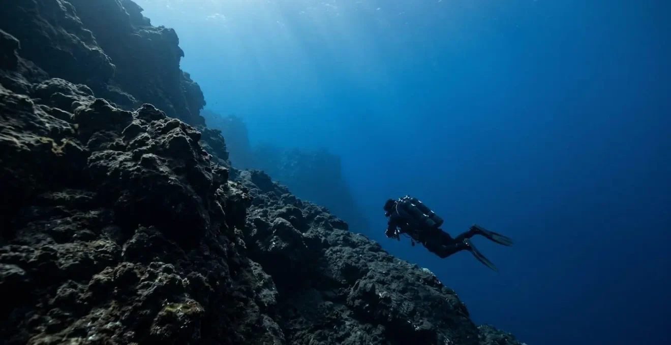 Technical diver with twin-tank configuration descending along volcanic drop-off in crystal-clear Atlantic waters
