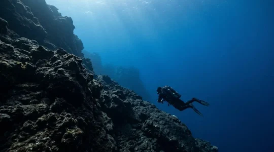 Technical diver with twin-tank configuration descending along volcanic drop-off in crystal-clear Atlantic waters